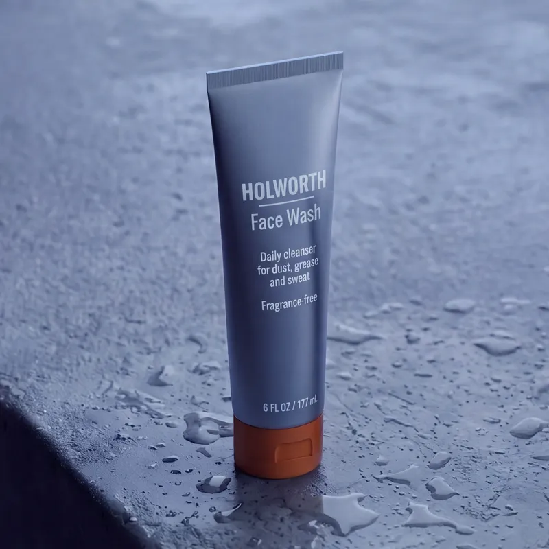 A tall steel-grey tube of Face Wash with an orange cap on grey concrete.
