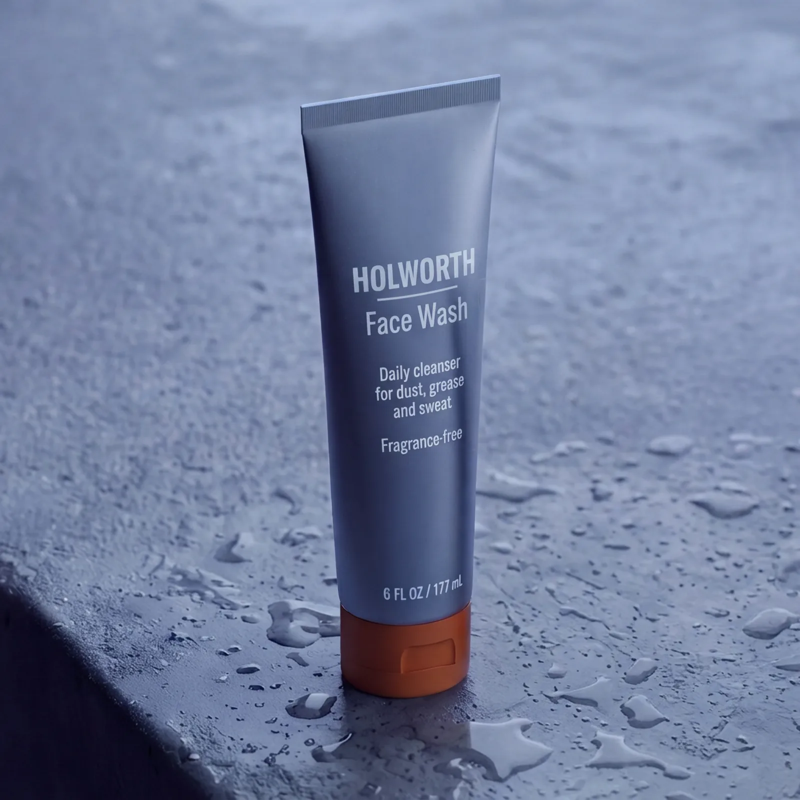Holworth Face Wash, a slate-grey container with an orange cap, labeled HOLWORTH, on grey concrete.