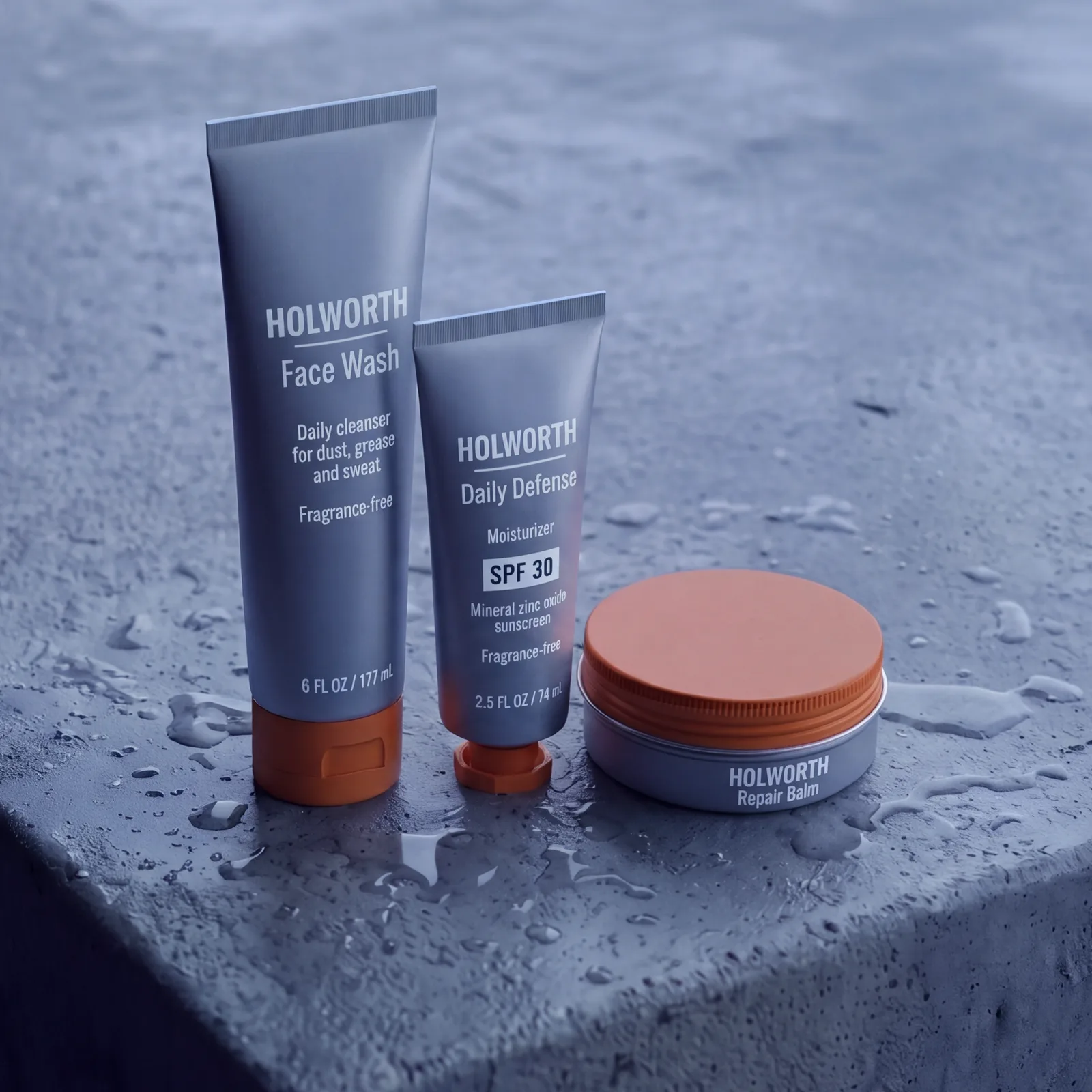 The Workday Kit on a wet concrete ledge: a tall tube of Face Wash, a short tube of Daily Defense SPF 30 and a tin of Repair Balm, steel grey with orange caps.
